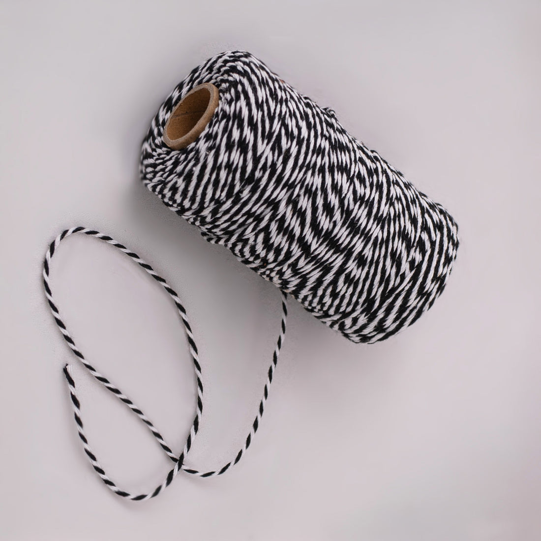 Roll of black and white striped butcher string, butcher twine, meat string, meat twine on a light gray background