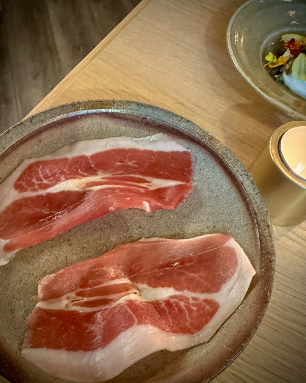 Raw meat slices on a ceramic plate with a blurred background, home made serrano, prociutto or parma ham